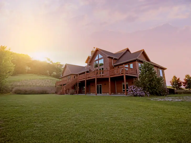 Grande pelouse dorée par le soleil couchant devant une maison de campagne en bois