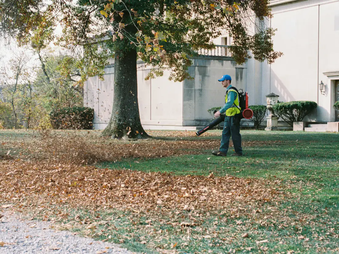 Ouvrier au souffleur dégageant les feuilles mortes d'une pelouse au grand ménage du printemps